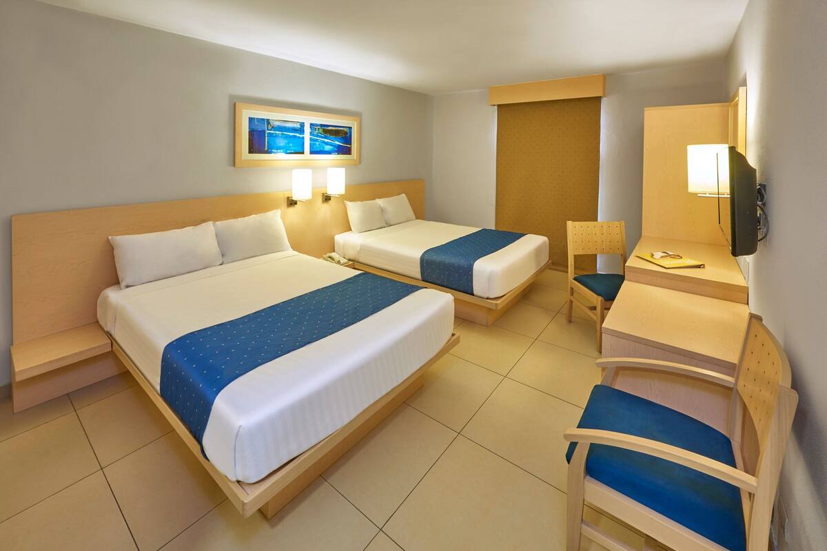 Ett hotellrum med två sängar, ett skrivbord, en stol, en TV och en tavla på väggen.
