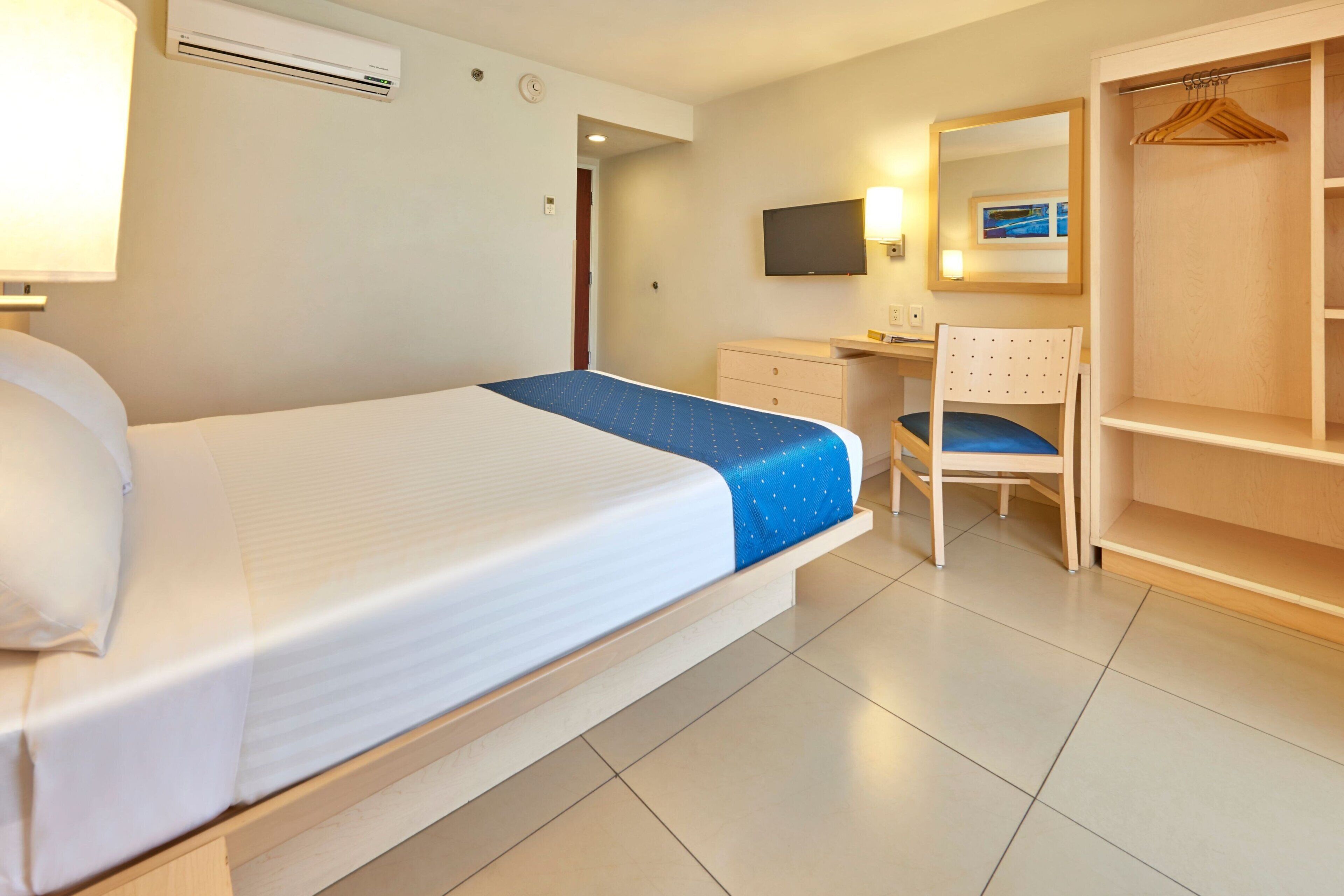 A hotel room with a bed, a desk, a chair, a wardrobe, and a TV.