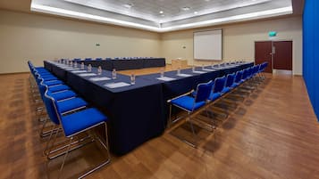Un salón de conferencias con una larga mesa, sillas azules y botellas de agua.