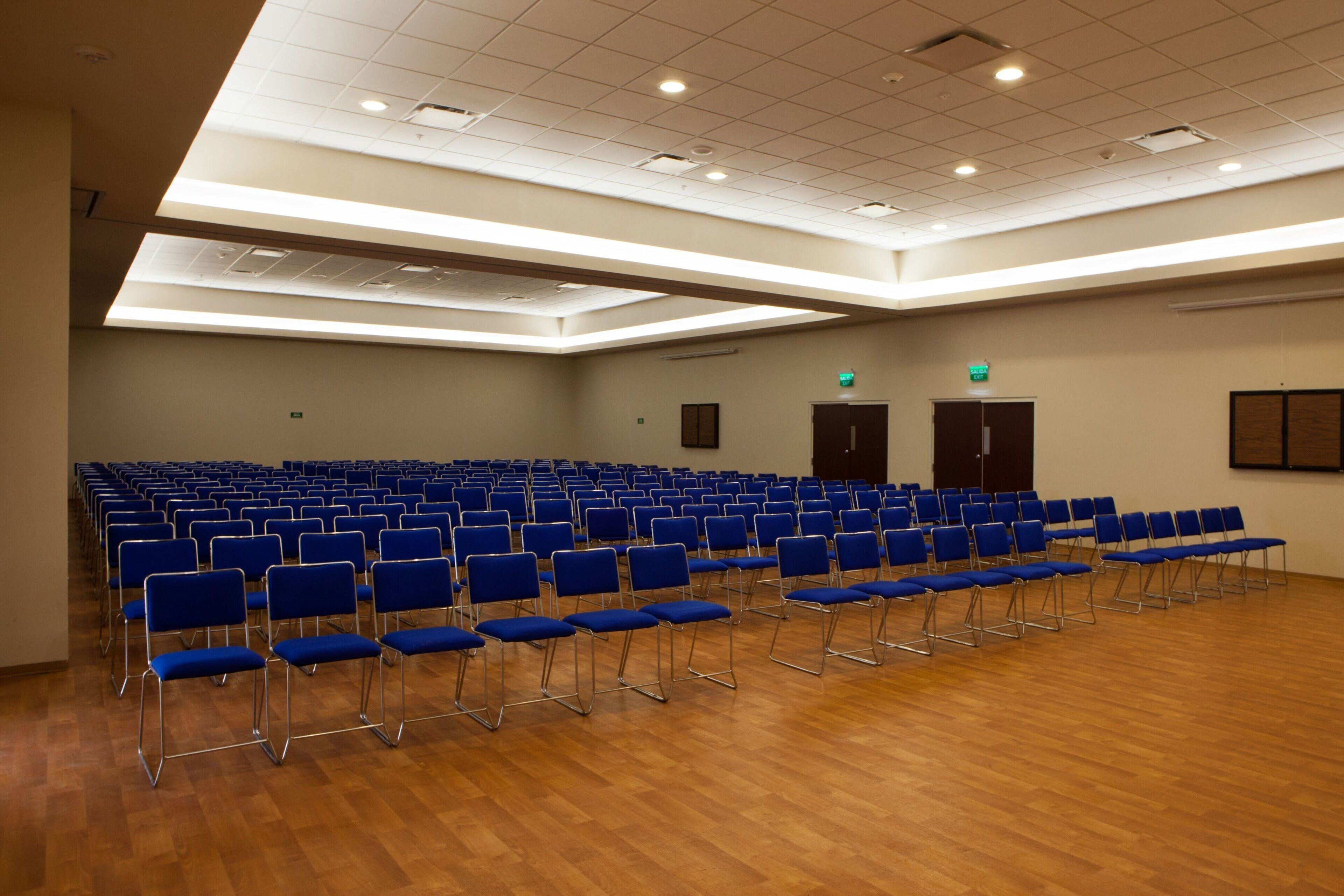 A large hall with rows of blue chairs and wooden flooring.