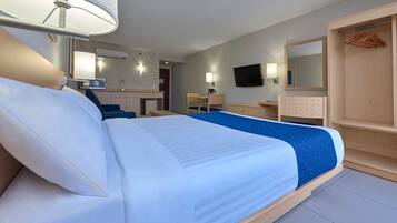 Habitación de hotel con una cama grande, un escritorio, una silla, un televisor, un espejo y un armario.