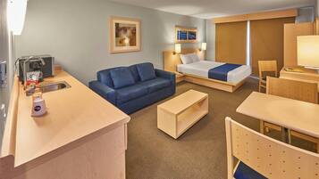 A hotel room with a bed, a sofa, a desk, a chair, a coffee machine, and a sink.