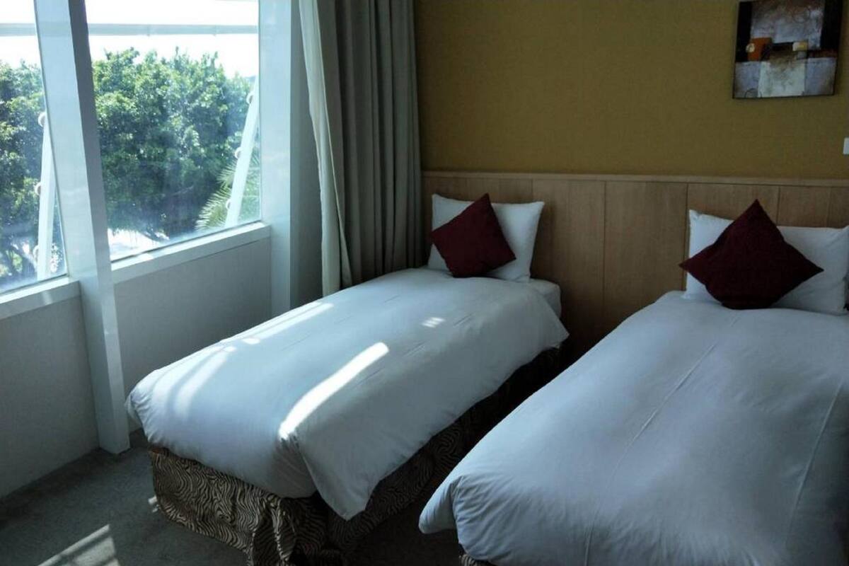 Habitación de hotel con dos camas, una ventana con cortinas y vistas a zonas verdes.