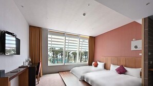 Habitació d'hotel amb llit, escriptori, televisió i finestra que dona a palmeres.