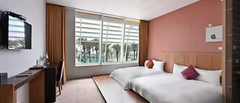 Una habitación de hotel con cama, escritorio, televisor y ventana con vista a palmeras.