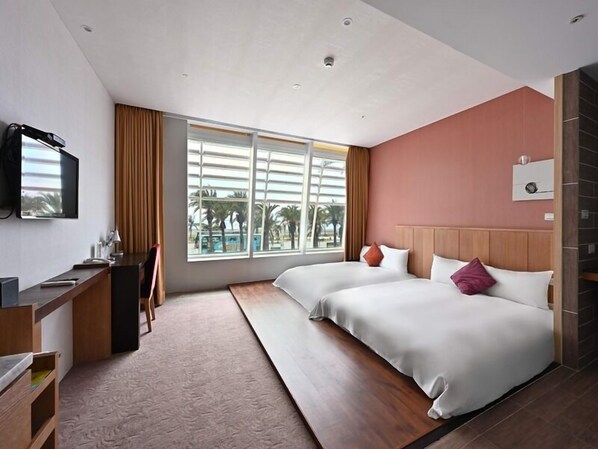 Une chambre d’hôtel équipée d’un lit, d’un bureau, d’une télévision et d’une fenêtre donnant sur des palmiers.