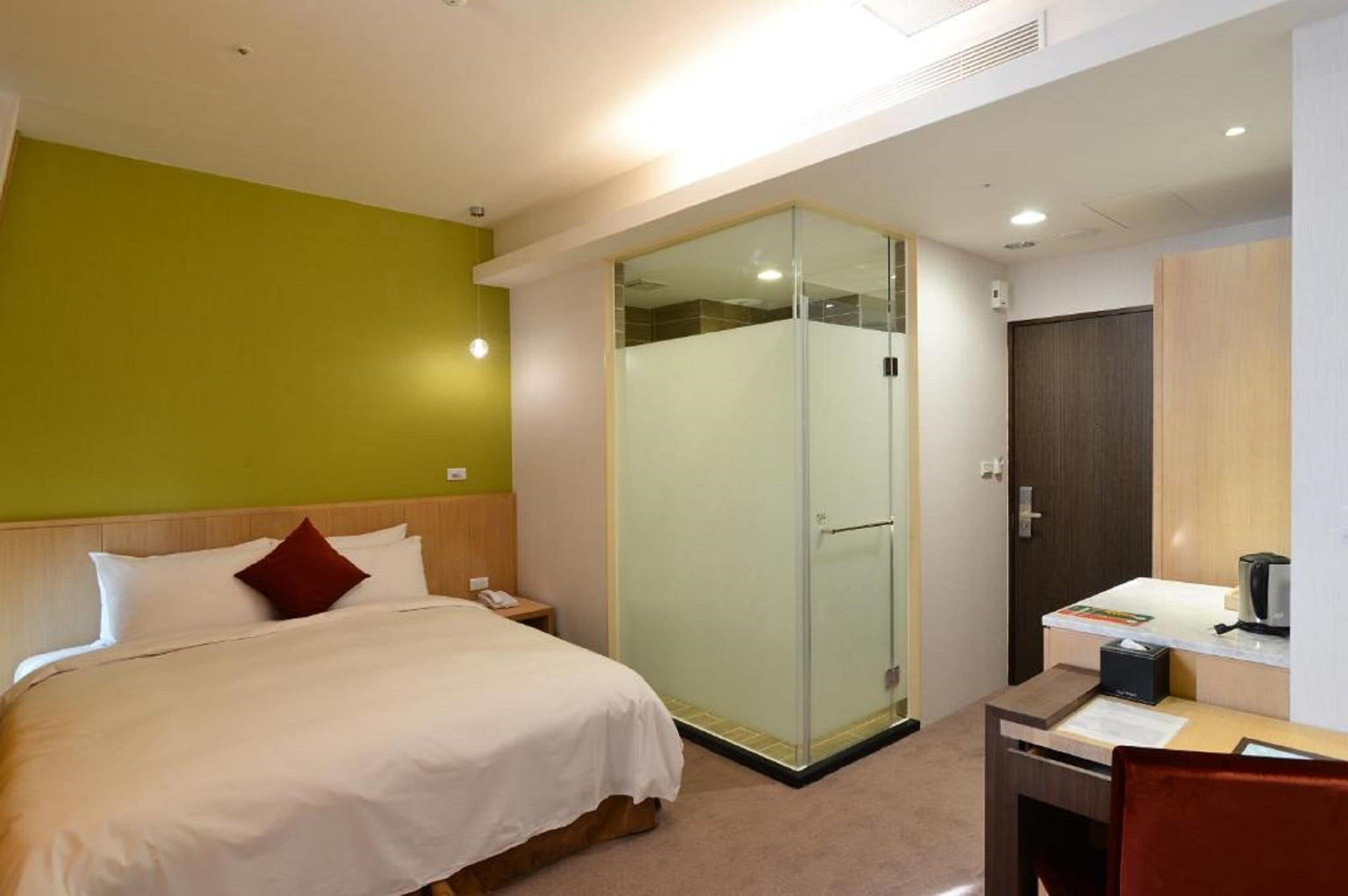 Camera d'albergo con un letto, una scrivania, un box doccia in vetro e un armadio.