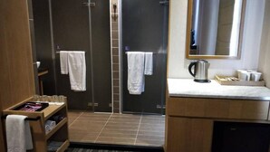Un bany modern amb dutxa, un lavabo amb mirall i una cafetera. Hi ha tovalloles penjades a la paret i una repisa amb productes de tocador.