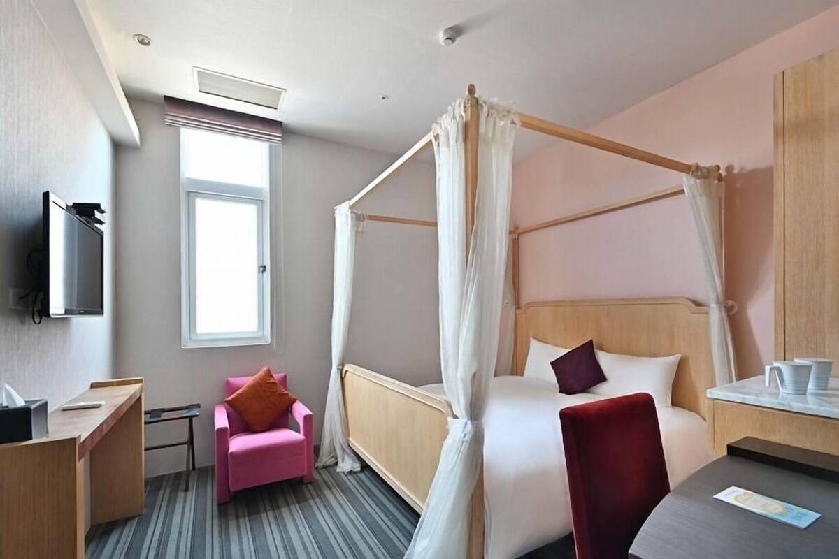 Una habitación de hotel con una cama con dosel, un escritorio, una silla, un televisor y una ventana.