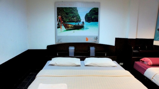 Habitación de hotel con cama, almohadas, una toalla doblada, un televisor y un cartel con un barco en la playa.