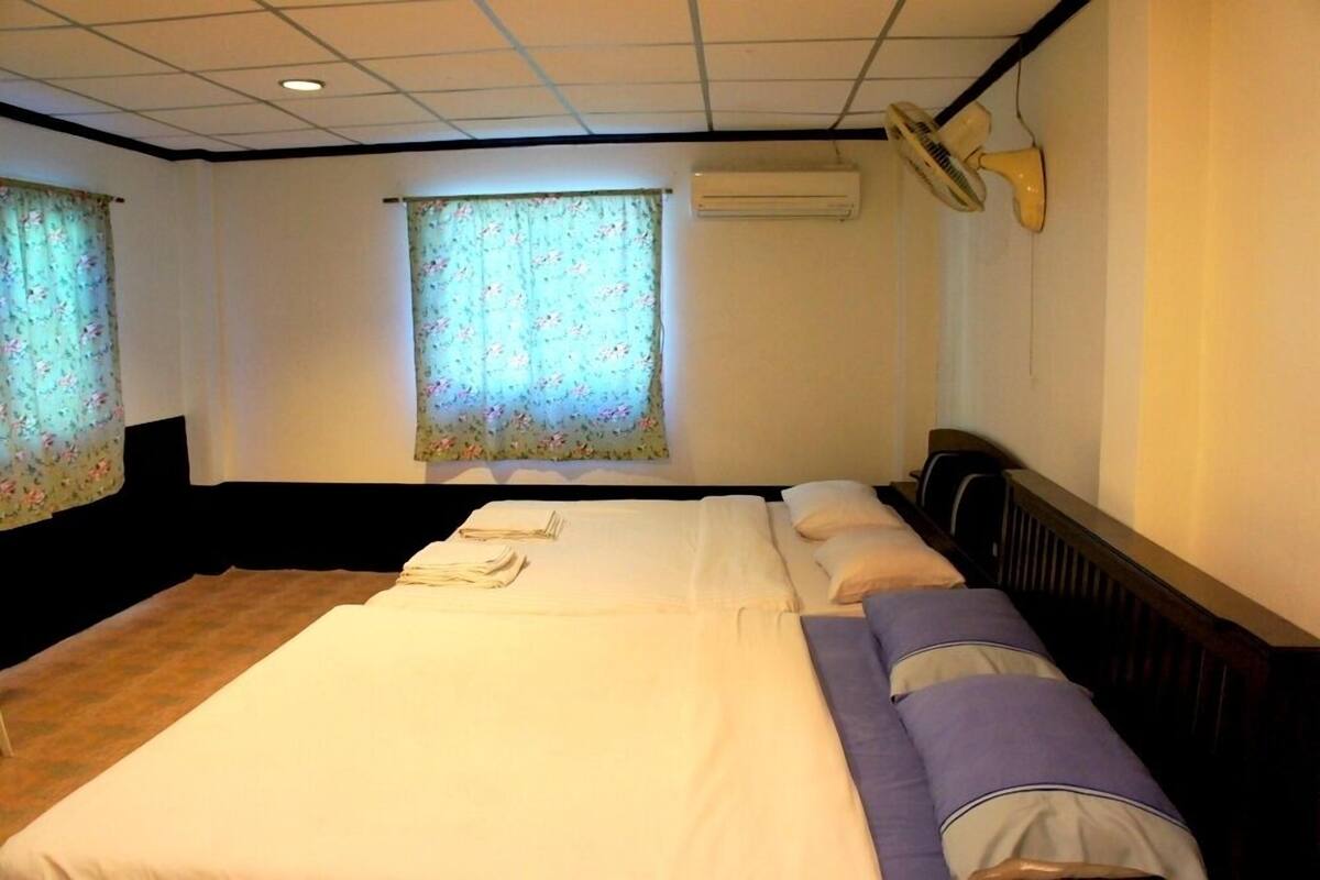 A hotel room with a large bed, a desk, a chair, a window with floral curtains, and a ceiling fan.