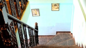 Una escalera con barandillas ornamentales, dos cuadros enmarcados en la pared y un suelo de baldosas.