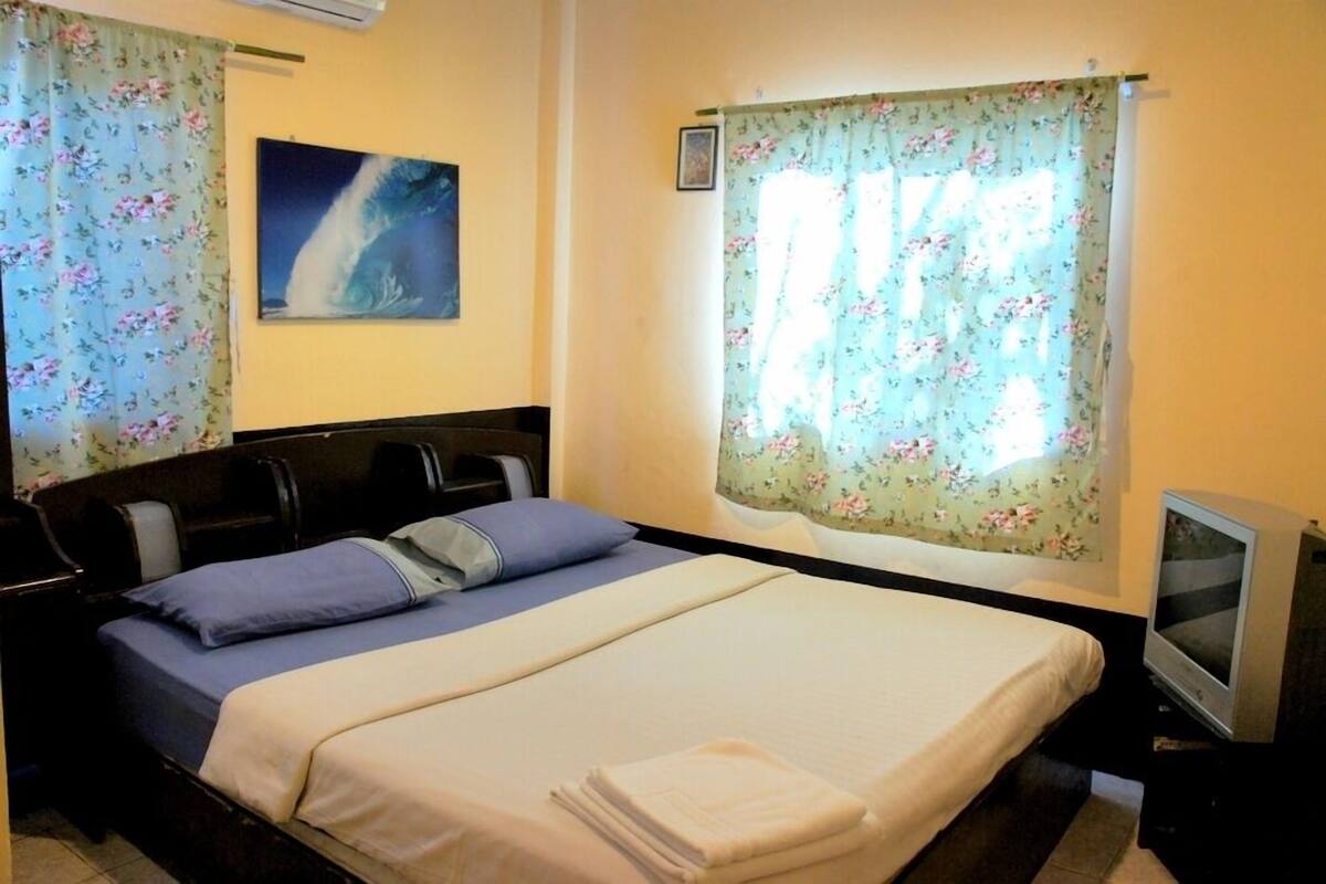 A hotel room with a bed, a television, and a painting on the wall.