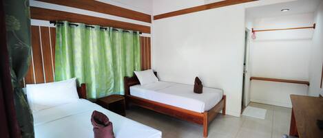 Habitación de hotel con dos camas individuales, cabecero de madera, cortina verde, aire acondicionado blanco y escritorio de madera.