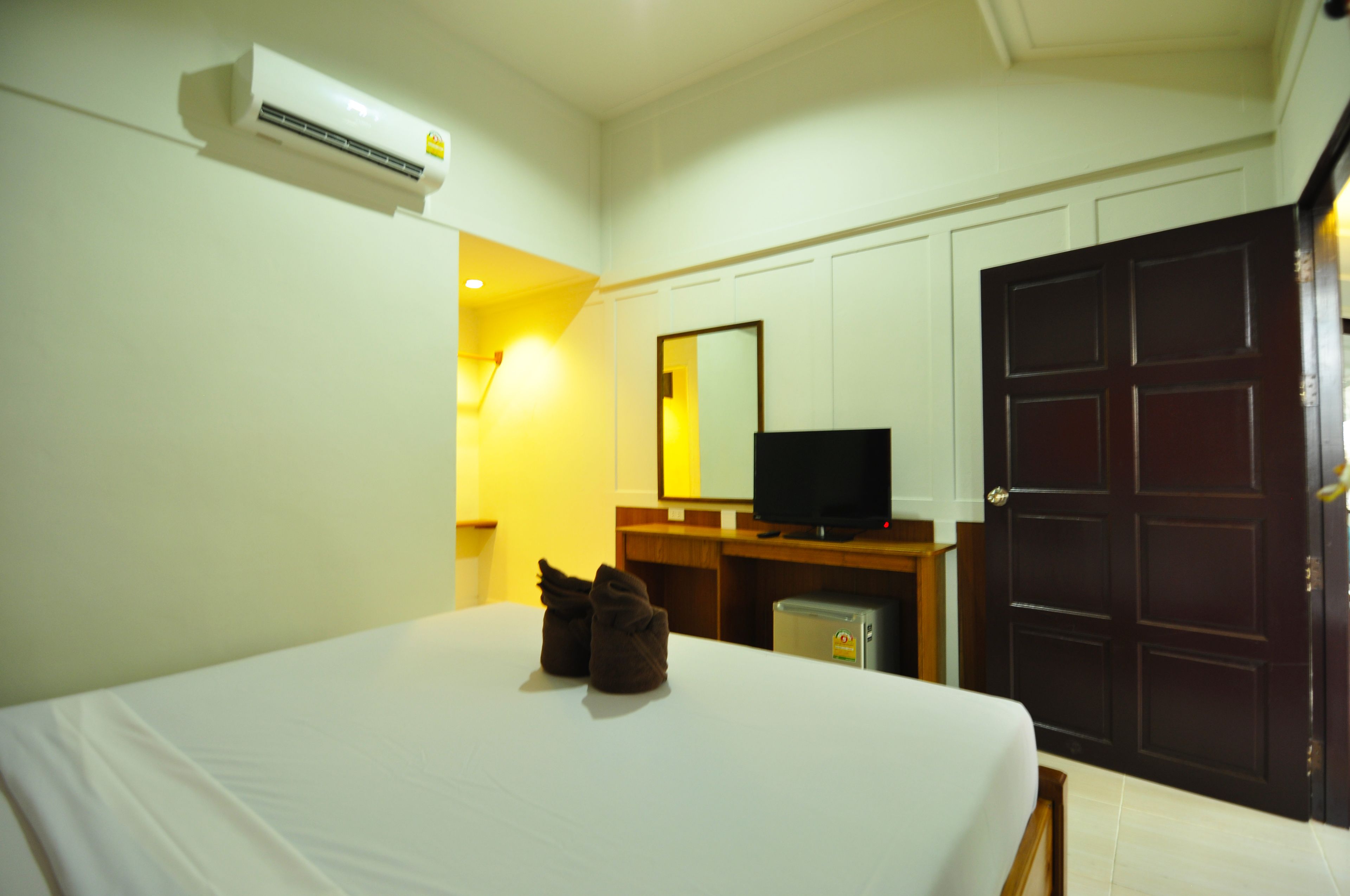 A hotel room with a bed, an air conditioner, a television, a desk, and a wardrobe.