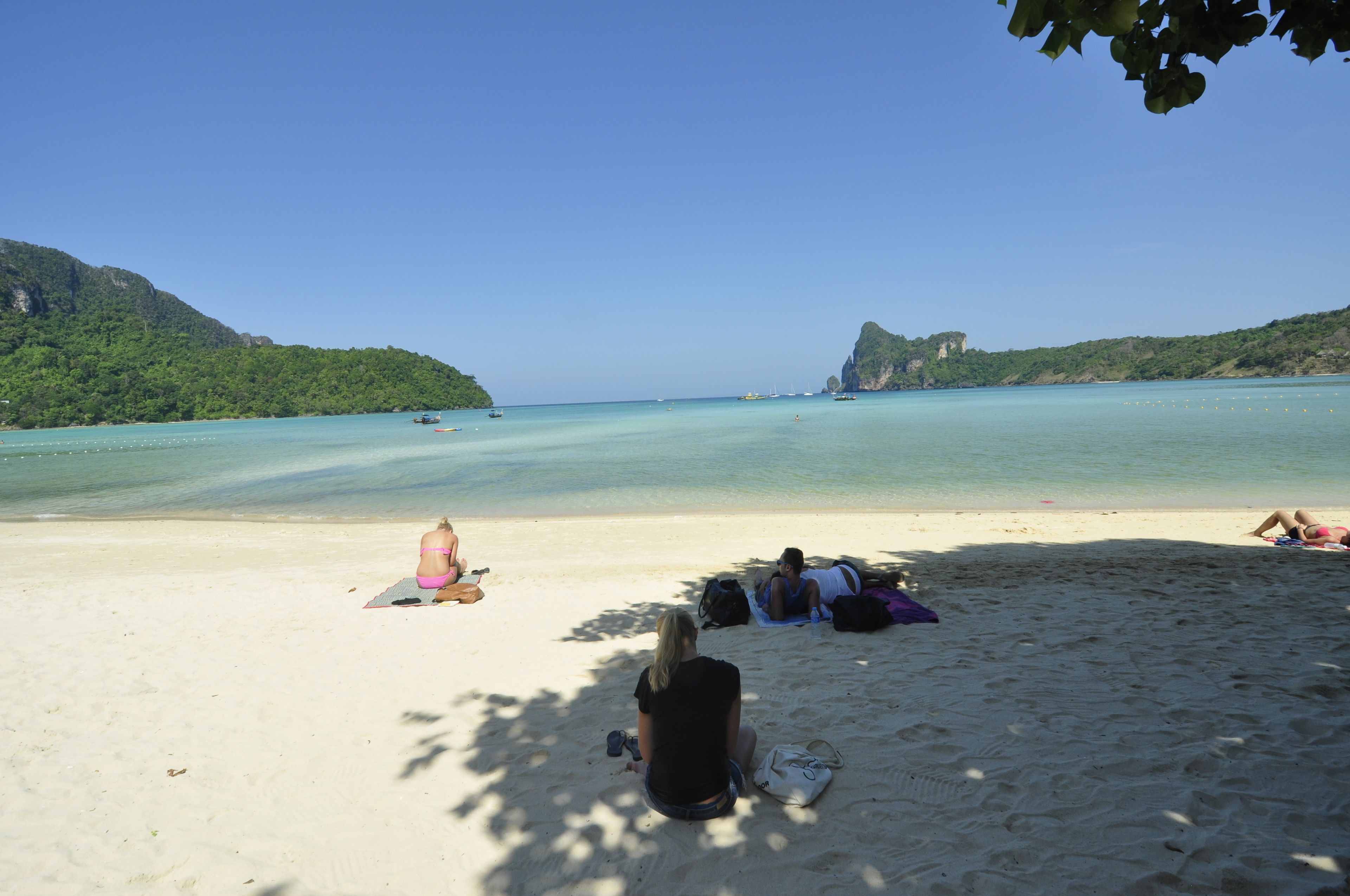 A beach with clear turquoise water, people relaxing on the sand, and a mountainous backdrop.