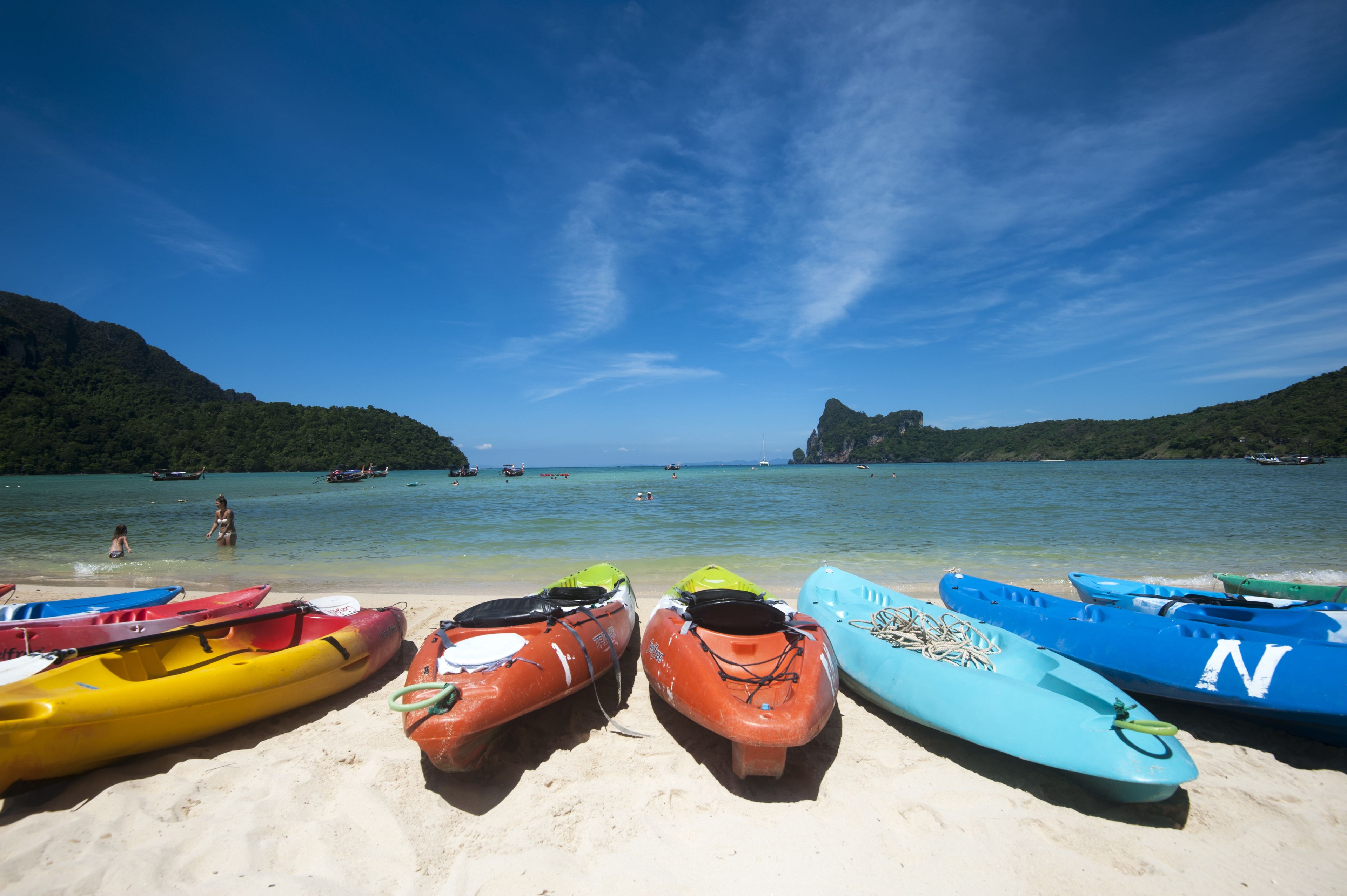 A beach with kayaks lined up on the sand, a clear blue sky, and a mountainous backdrop.