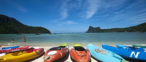 A beach with kayaks lined up on the sand, a clear blue sky, and a mountainous backdrop.