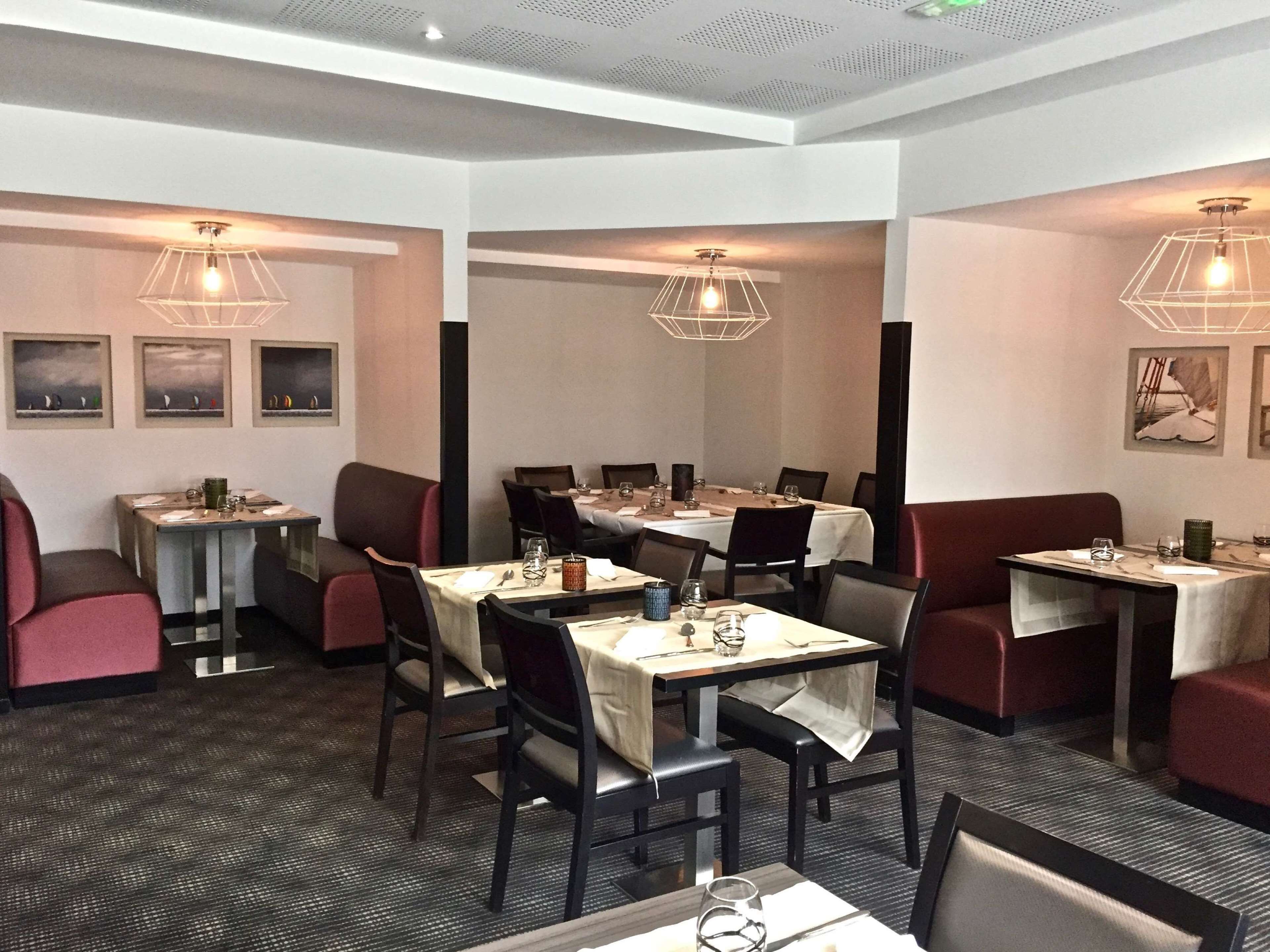Un restaurant doté de nombreuses tables et de banquettes, chacune étant recouverte d’une nappe blanche et agrémentée de chaises foncées.