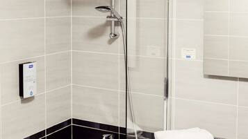 A modern bathroom with a glass-enclosed shower, a black and white tiled wall, and a white sink with a towel on the counter.