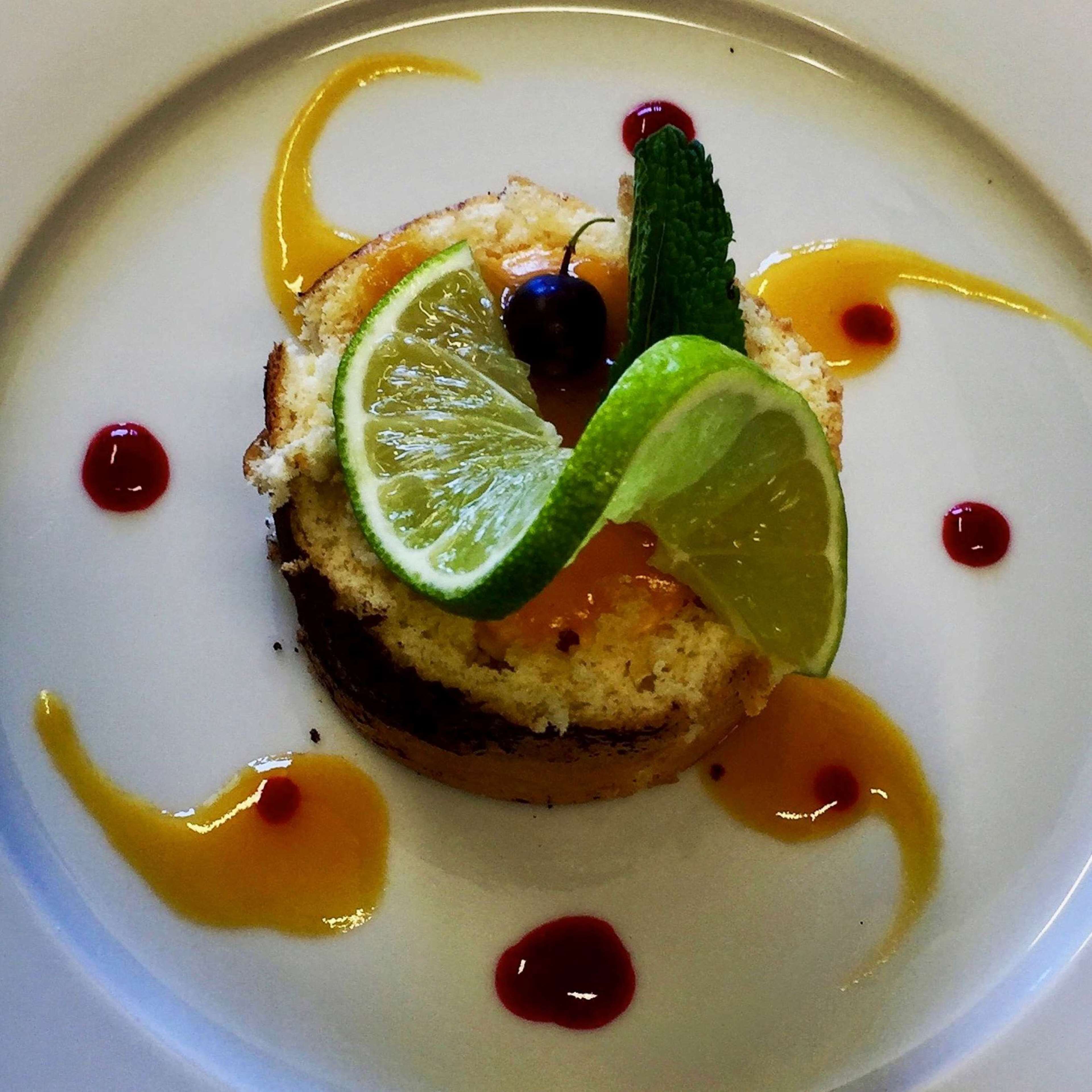 A dessert with lime and mint garnish on a white plate with sauce drizzles.