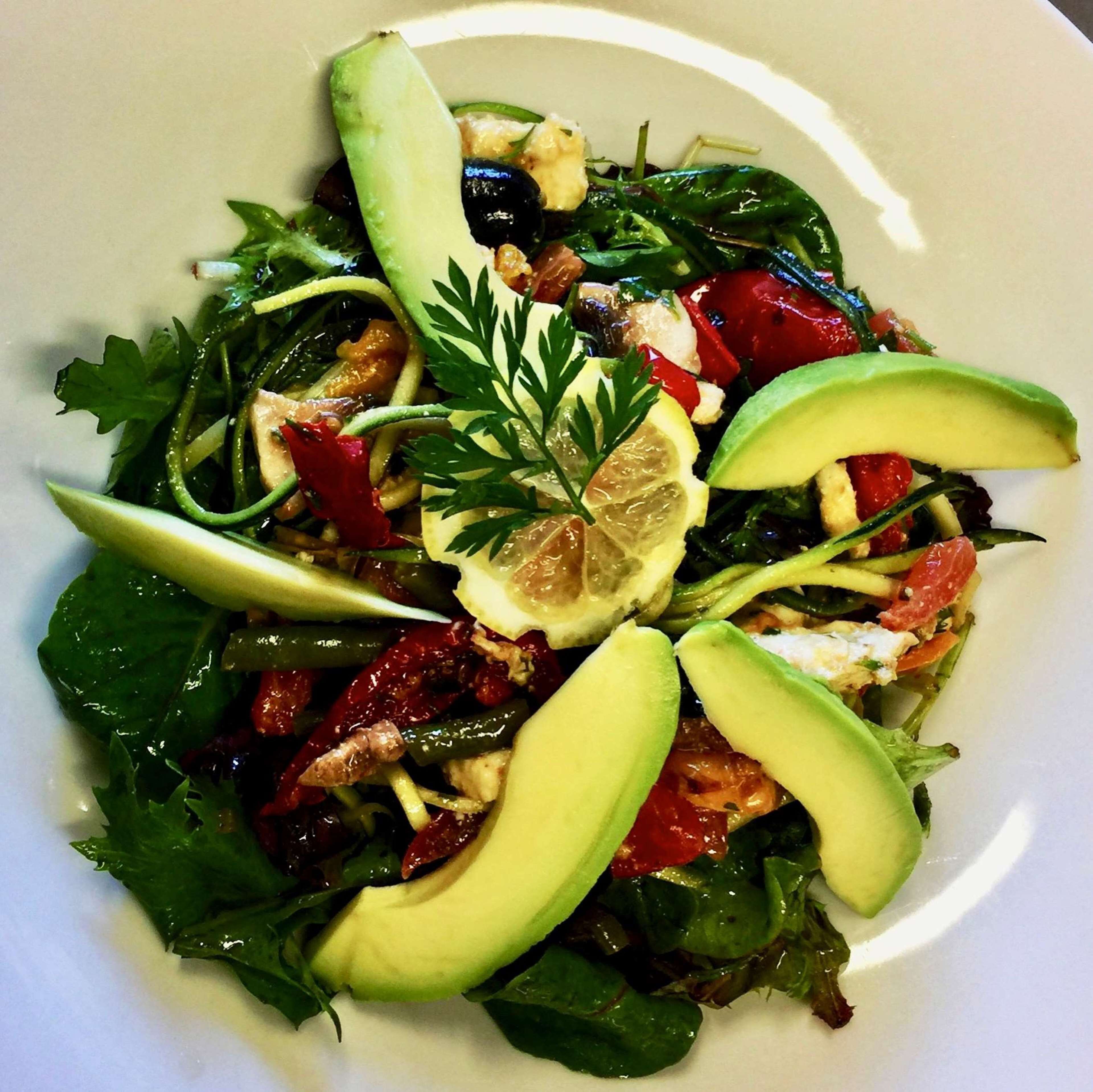 A plate of mixed greens salad with avocado slices, cherry tomatoes, and nuts.