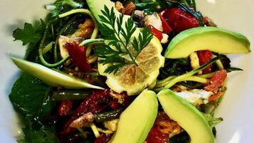A plate of mixed greens salad with avocado slices, cherry tomatoes, and nuts.