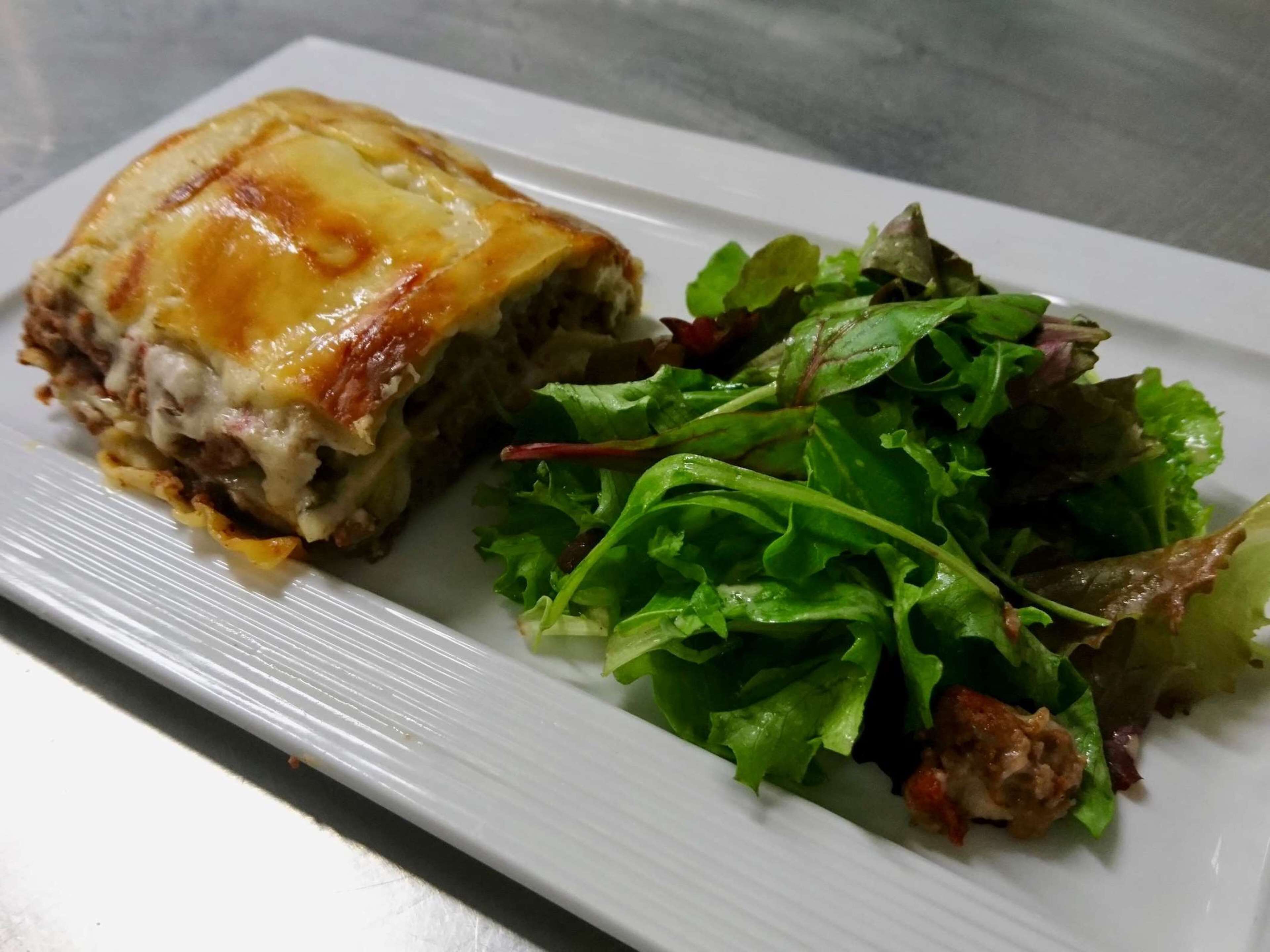 A plate with a slice of lasagna and a side salad.