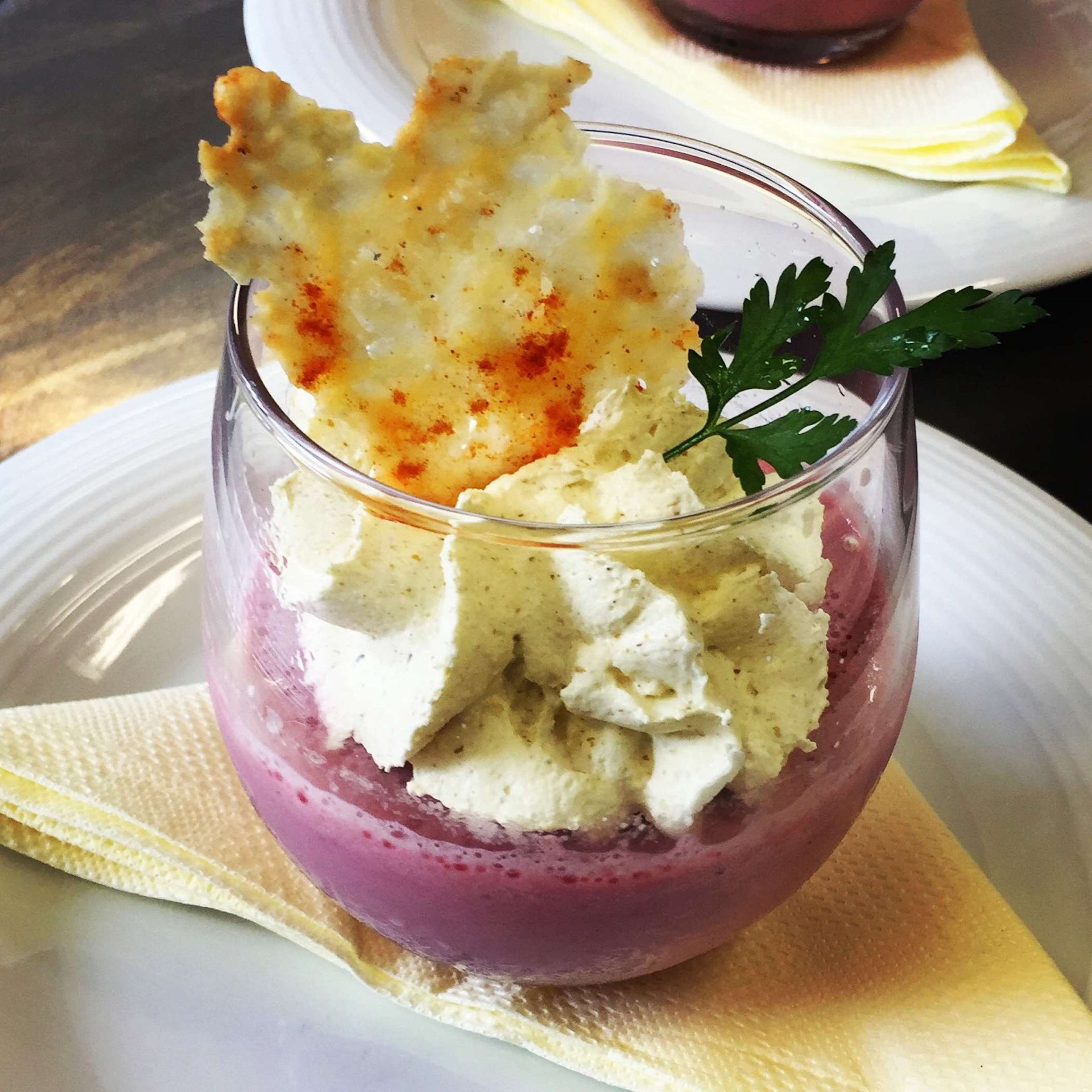 A dessert in a glass with whipped cream and a piece of fried food on top, garnished with a leaf.