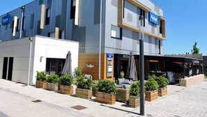 Un edificio moderno con un restaurante llamado 'Restavle' en la planta baja, mesas al aire libre con sombrillas y un cartel que dice 'Kyrid'.
