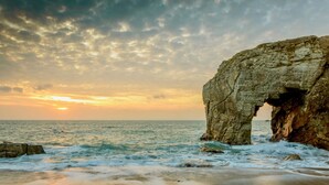 Paisaje costero con una formación rocosa destacada que presenta un arco.