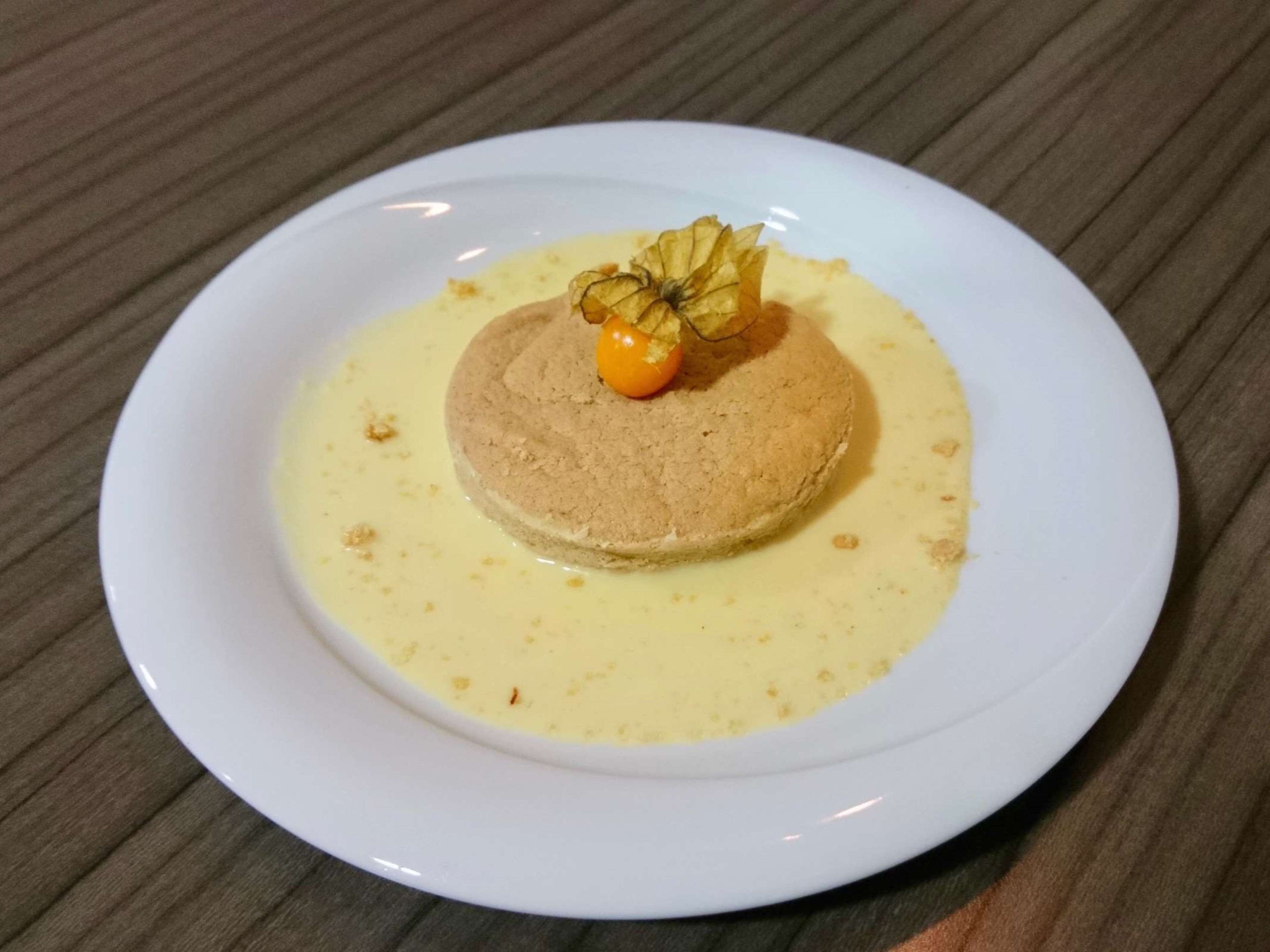 A dessert on a white plate with a creamy sauce and a cherry on top.
