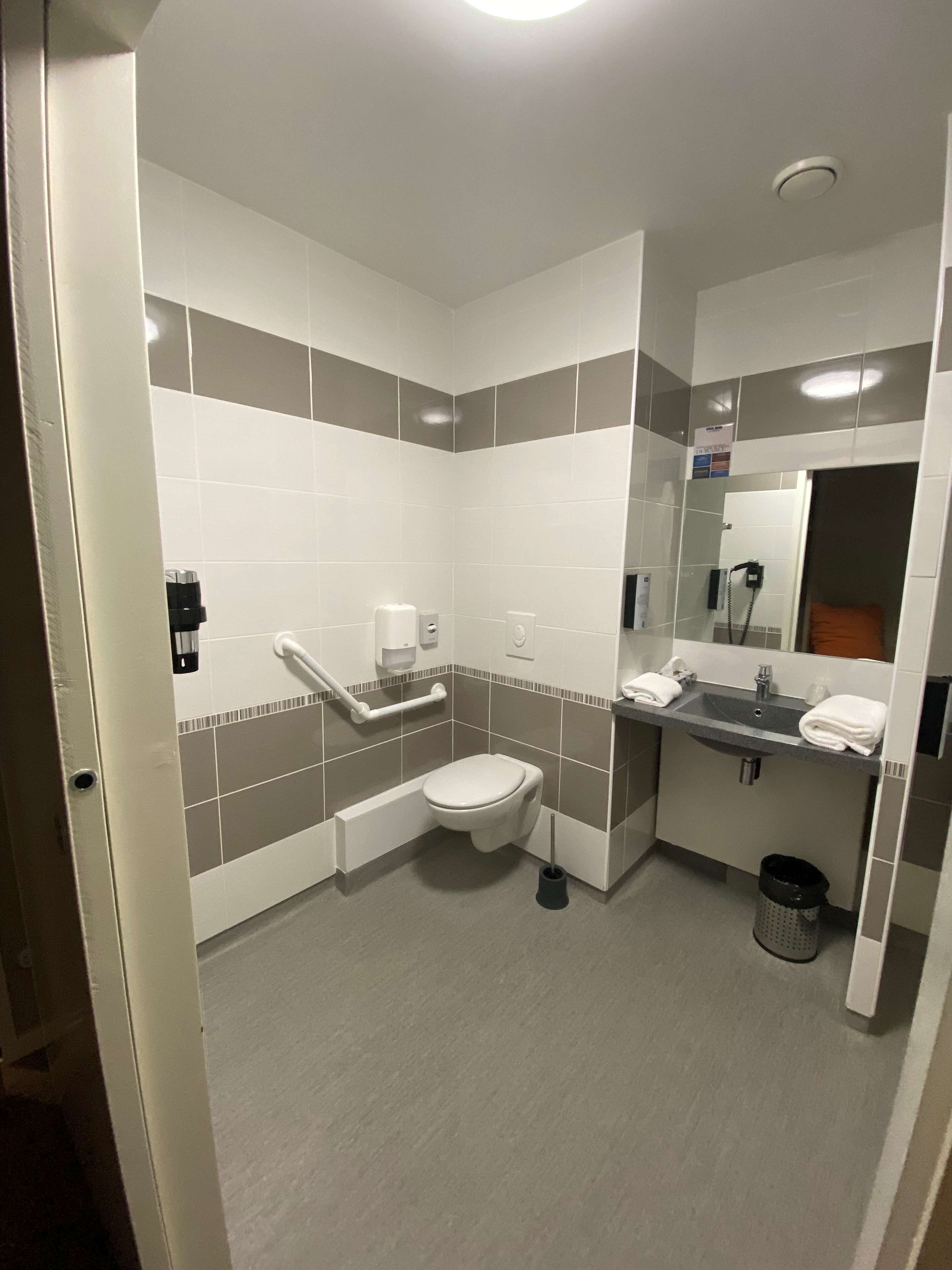 Une salle de bain moderne équipée de toilettes, d’un lavabo et d’un sèche-mains.