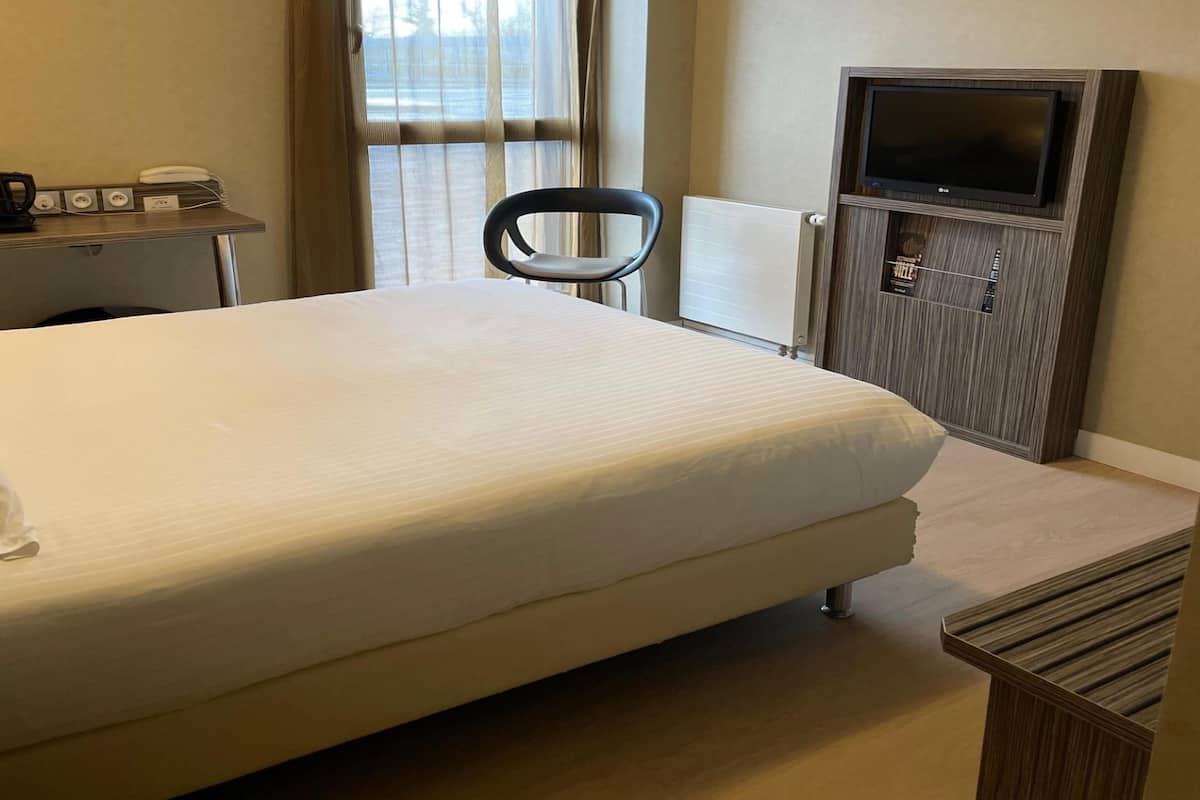 Ein Hotelzimmer mit einem großen Bett, einem Schreibtisch mit Telefon, einem Sessel, einem Fernseher und einer Heizung.