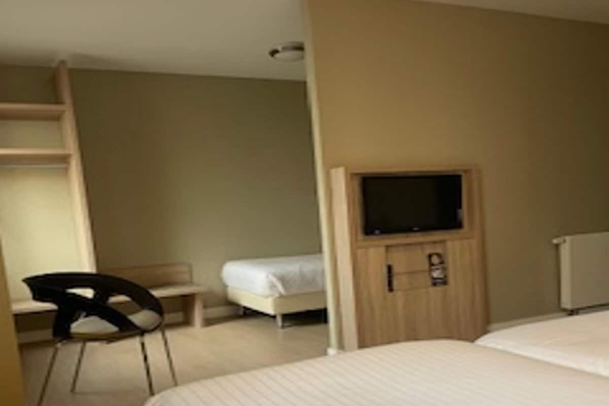 Ein Schlafzimmer mit Bett, Sessel, Schreibtisch, Fernseher und Kleiderschrank.