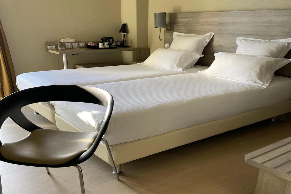 Ein Hotelzimmer mit Doppelbett, Nachttisch mit Lampe, Stuhl und kleinem Tisch mit Tablett.