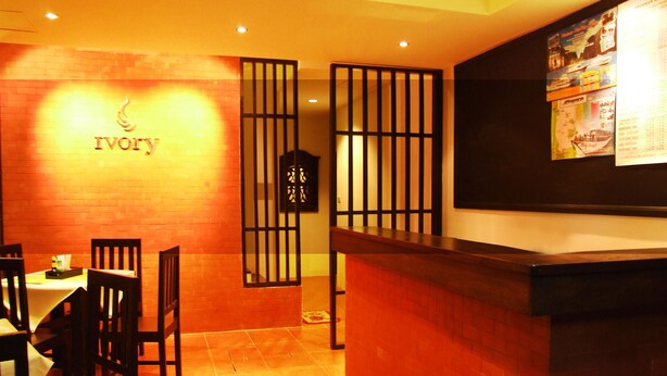 Interior de restaurante con mostrador de recepción de madera, una mesa con sillas y una pared con el nombre 'Ivory'.