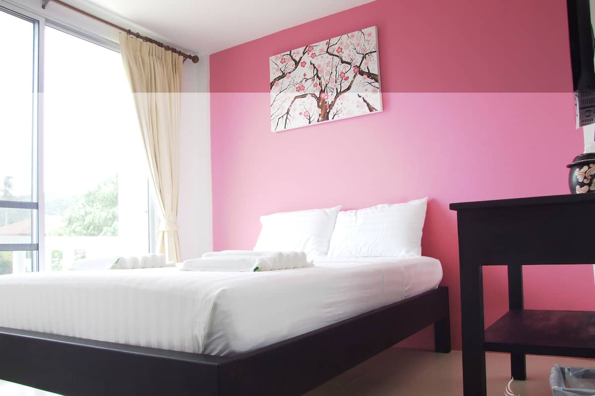 A bedroom with a bed, a nightstand, a window with curtains, and a pink wall with a floral painting.