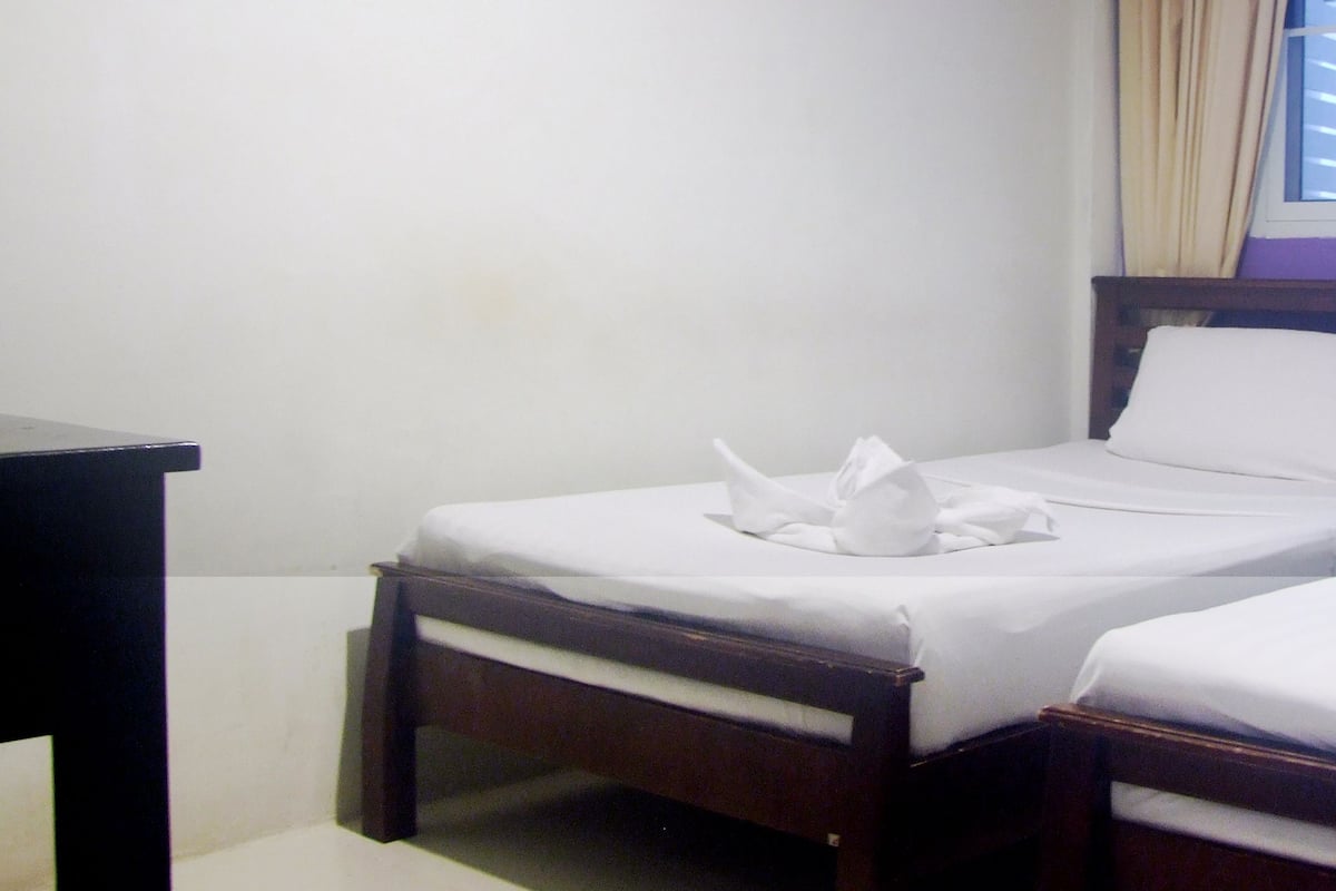 A room with two single beds, a wooden nightstand, and a window with blinds.