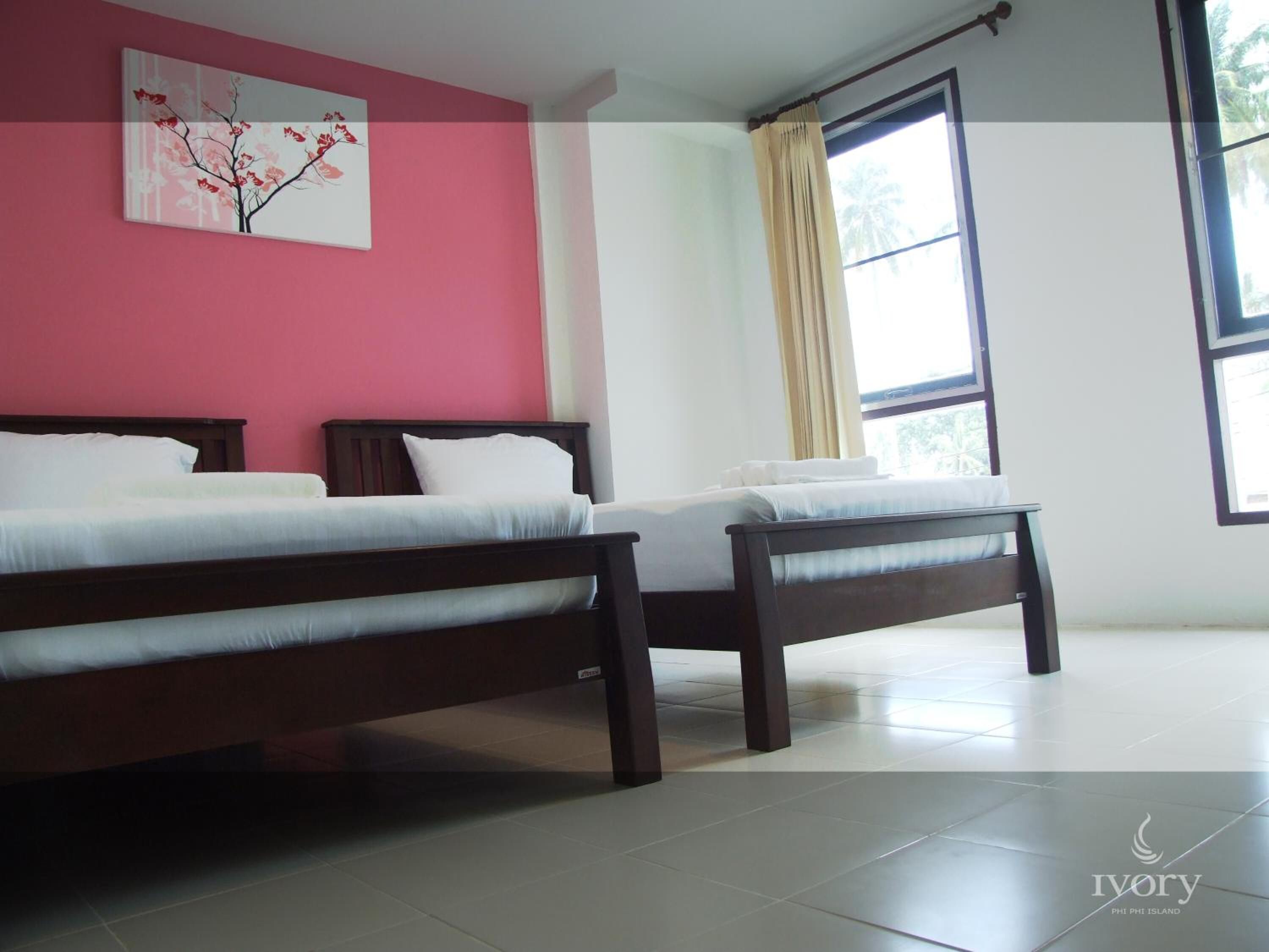 A bedroom with two beds, a window with curtains, and a pink wall with a floral painting.