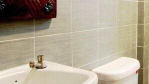 Un baño con lavamanos y retrete blancos, paredes con azulejos y un toallero rojo.