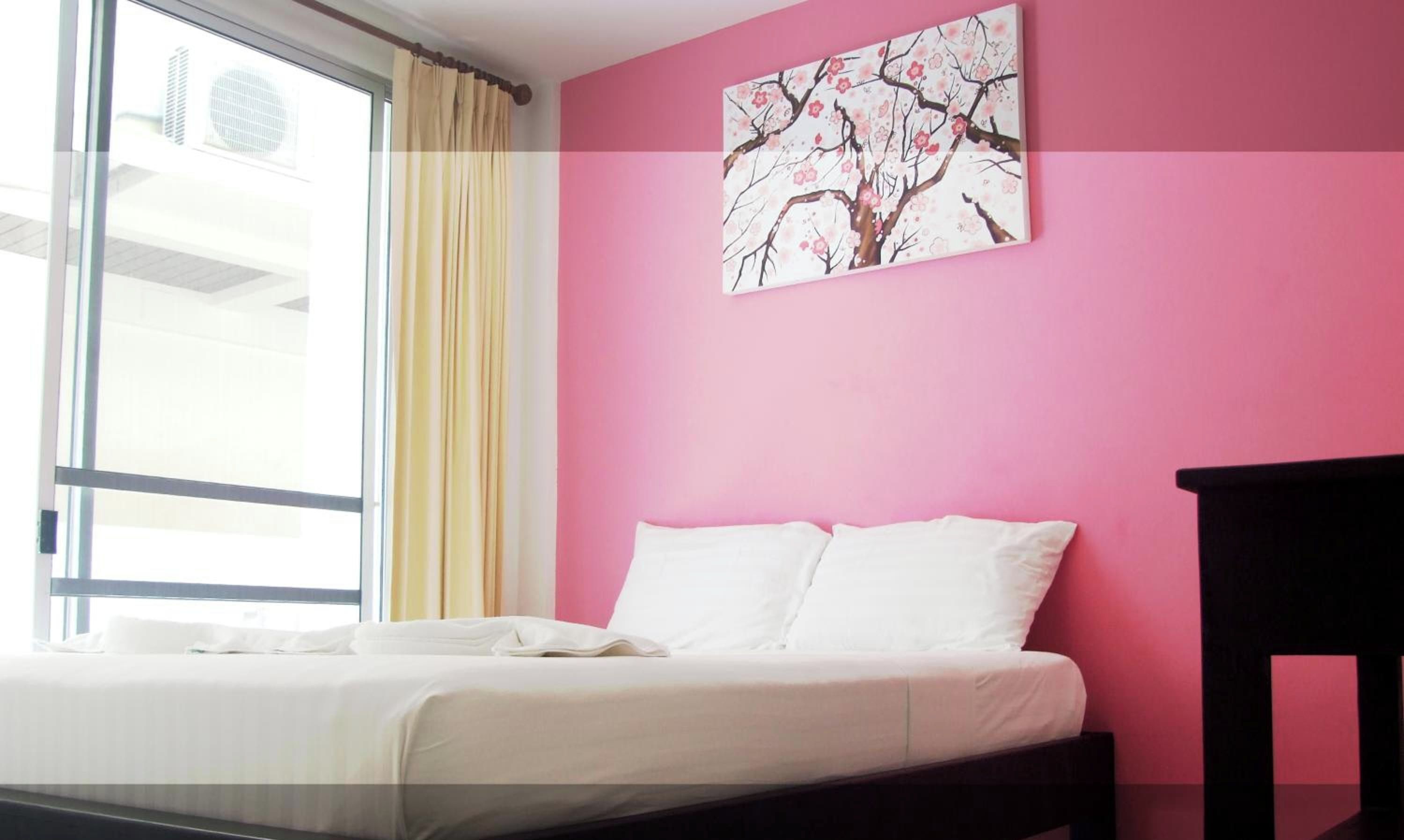 A hotel room with a bed, a window with curtains, and a wall with a painting.