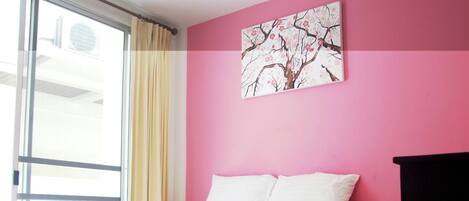 A hotel room with a bed, a window with curtains, and a wall with a painting.