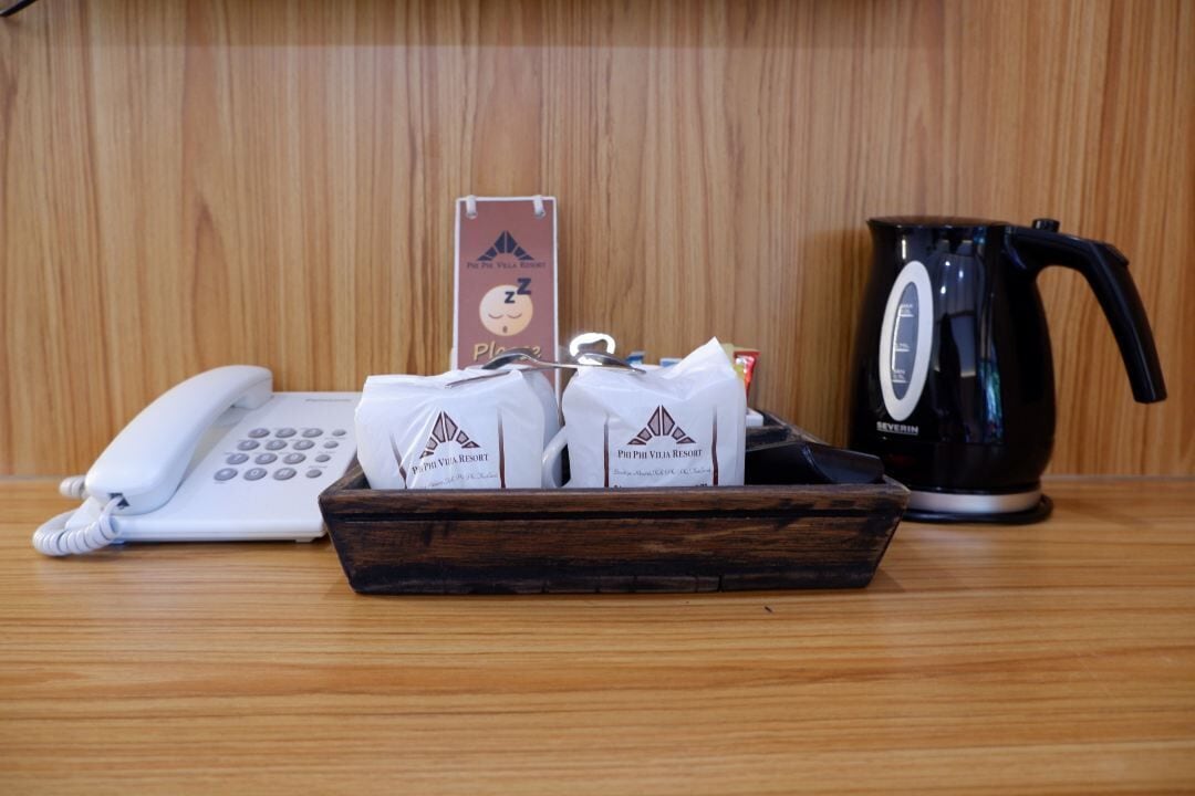 A wooden table with a white telephone, a black coffee pot, and a tray with bags labeled "Piphi Villa Resort".
