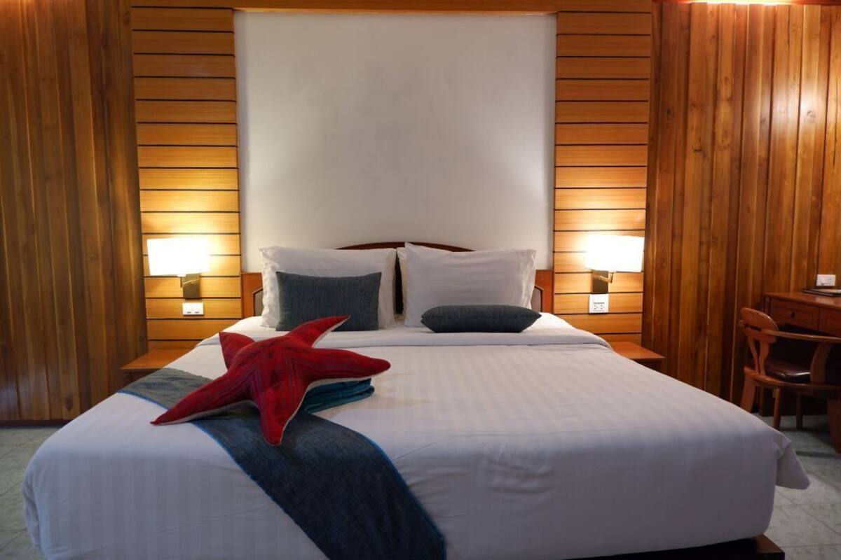 Een net opgemaakt bed met witte lakens, twee kussens en een rode zeester decoratie. Aan beide zijden van het bed hangen twee wandlampen.