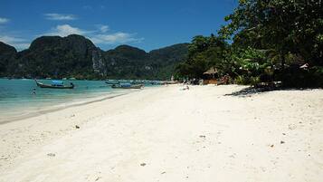 A beach with clear turquoise water, boats, and lush greenery.