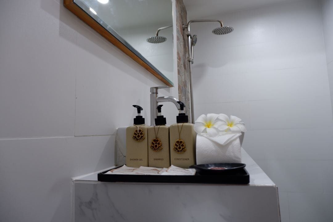A bathroom with a white tiled wall, a mirror, a showerhead, and a sink with toiletries.