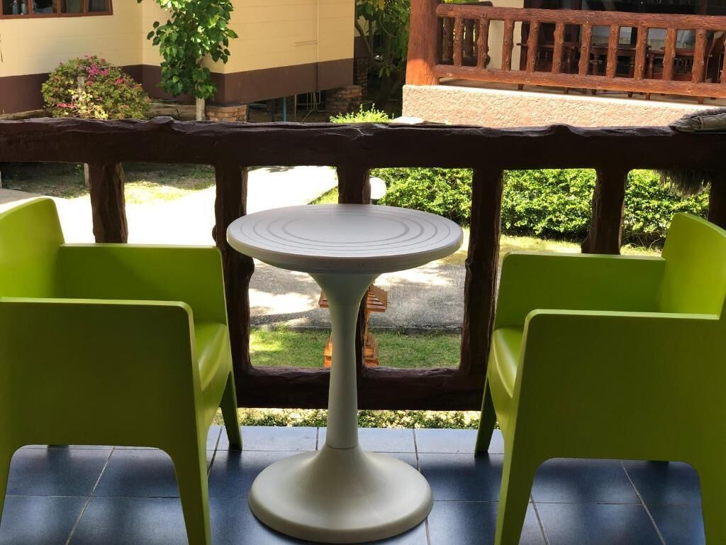 Un balcon avec une table ronde et deux chaises vertes.
