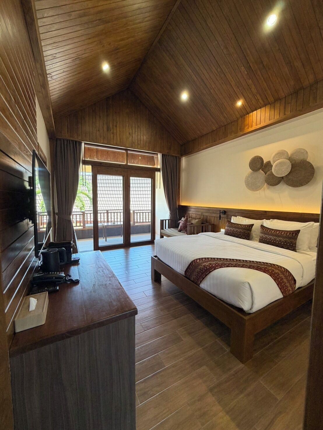 A spacious bedroom with a large bed, wooden ceiling, and a TV on a wooden desk.