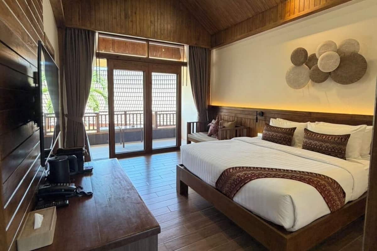 Een ruime slaapkamer met een groot bed, houten plafond en een televisie op een houten bureau.